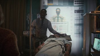 Movie still from “Hotel Artemis” (2018), directed by Drew Pearce – A man standing next to a man laying on a bed; Medium shot, Over the shoulder angle