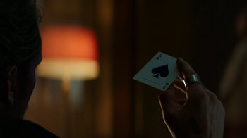 Movie still from “Hotel Artemis” (2018), directed by Drew Pearce – A person holding up a playing card in front of a lamp; Close Up shot, Over the shoulder angle