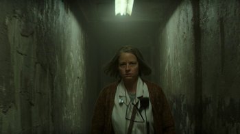 Movie still from “Hotel Artemis” (2018), directed by Drew Pearce – A woman with a stethoscope standing in a dark hallway; Medium shot, Low angle