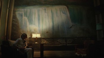 Movie still from “Hotel Artemis” (2018), directed by Drew Pearce – A woman sitting in front of a painting of a waterfall; Wide shot, Low angle