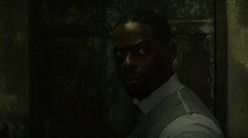 Movie still from “Hotel Artemis” (2018), directed by Drew Pearce – A man in a suit and tie in front of a brick wall; Close Up shot, Over the shoulder angle