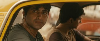 Movie still from “Hotel Mumbai” (2018), directed by Anthony Maras – A man sitting in the back seat of a car; Close Up shot, Over the shoulder angle