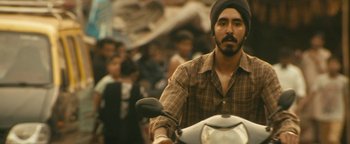 Movie still from “Hotel Mumbai” (2018), directed by Anthony Maras – A man riding a motorcycle down a street; Medium shot, Low angle