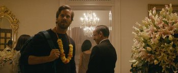 Movie still from “Hotel Mumbai” (2018), directed by Anthony Maras – A man wearing a lei standing next to a man in a suit; Medium shot, Over the shoulder angle