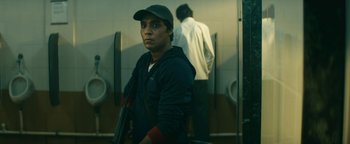 Movie still from “Hotel Mumbai” (2018), directed by Anthony Maras – A man in a hat is standing in a bathroom; Medium shot, Low angle