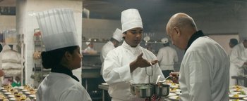 Movie still from “Hotel Mumbai” (2018), directed by Anthony Maras – A man in a chef's hat is stirring a pot; Medium shot, Over the shoulder angle