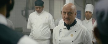 Movie still from “Hotel Mumbai” (2018), directed by Anthony Maras – A man in a chef's outfit standing next to another man in a kitchen; Close Up shot, Over the shoulder angle