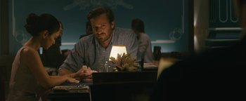 Movie still from “Hotel Mumbai” (2018), directed by Anthony Maras – A man sitting at a table with a candle in the middle of the room; Medium shot, Over the shoulder angle