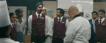Movie still from “Hotel Mumbai” (2018), directed by Anthony Maras – A group of men standing next to each other in a kitchen; Medium shot, Over the shoulder angle