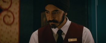 Movie still from “Hotel Mumbai” (2018), directed by Anthony Maras – A man with a beard wearing a black tie and a maroon vest; Close Up shot, Over the shoulder angle
