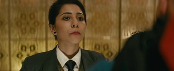 Movie still from “Hotel Mumbai” (2018), directed by Anthony Maras – A woman wearing a suit and tie looking to her left; Close Up shot, Over the shoulder angle