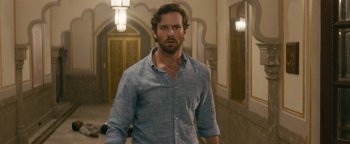 Movie still from “Hotel Mumbai” (2018), directed by Anthony Maras – A man standing in front of a door wearing a blue shirt; Medium shot, Over the shoulder angle