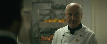 Movie still from “Hotel Mumbai” (2018), directed by Anthony Maras – An older man wearing a white chef's outfit; Close Up shot, Over the shoulder angle