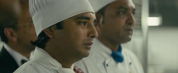 Movie still from “Hotel Mumbai” (2018), directed by Anthony Maras – Two men in white hats and ties looking to their left; Close Up shot, Over the shoulder angle