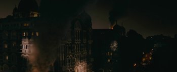 Movie still from “Hotel Mumbai” (2018), directed by Anthony Maras – A building that is lit up in the dark; Extreme Wide shot, High angle