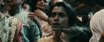 Movie still from “Hotel Mumbai” (2018), directed by Anthony Maras – A group of people standing around a woman; Close Up shot, Over the shoulder angle