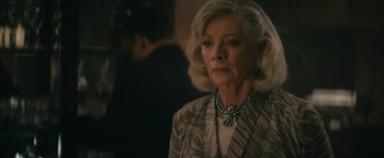 Movie still from “Hotel Mumbai” (2018), directed by Anthony Maras – An older woman wearing a necklace and a jacket; Close Up shot, Over the shoulder angle