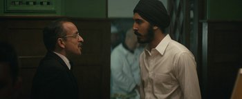 Movie still from “Hotel Mumbai” (2018), directed by Anthony Maras – A man in a turban talking to another man in glasses; Medium shot, Over the shoulder angle