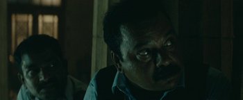 Movie still from “Hotel Mumbai” (2018), directed by Anthony Maras – A person sitting down with his eyes wide open; Close Up shot, Low angle