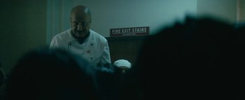 Movie still from “Hotel Mumbai” (2018), directed by Anthony Maras – A man wearing a chef's outfit in a kitchen; Medium shot, Low angle