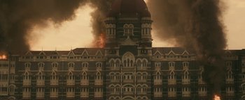 Movie still from “Hotel Mumbai” (2018), directed by Anthony Maras – A large building with smoke billowing out of it; Extreme Wide shot, High angle