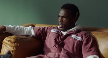 Movie still from “House Party” (2023), directed by Calmatic – A man sitting on top of a couch in a room; Close Up shot, High angle