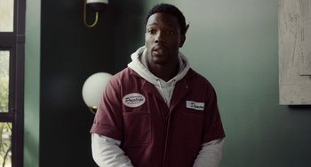 Movie still from “House Party” (2023), directed by Calmatic – A man in a maroon jacket standing in front of a green wall; Medium shot, Over the shoulder angle