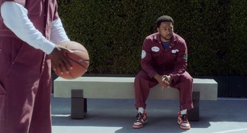 Movie still from “House Party” (2023), directed by Calmatic – A man sitting on a bench with a basketball in front of him; Medium shot, Over the shoulder angle