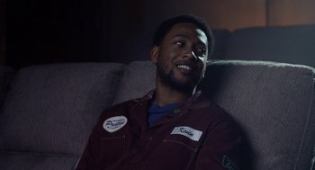 Movie still from “House Party” (2023), directed by Calmatic – A man sitting on a couch smiling at the camera; Close Up shot, Over the shoulder angle