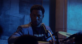 Movie still from “House Party” (2023), directed by Calmatic – A man sitting in front of microphones in a dark room; Medium shot, Over the shoulder angle