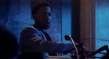 Movie still from “House Party” (2023), directed by Calmatic – A man sitting in front of a microphone in a room; Close Up shot, Over the shoulder angle