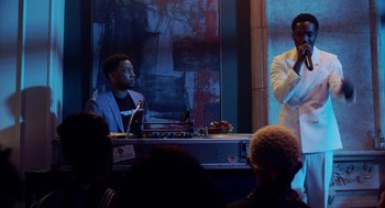 Movie still from “House Party” (2023), directed by Calmatic – Two men are sitting in front of an audience; Medium shot, Over the shoulder angle