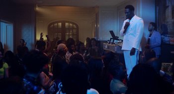 Movie still from “House Party” (2023), directed by Calmatic – A crowd of people sitting in a living room; Wide shot, Over the shoulder angle
