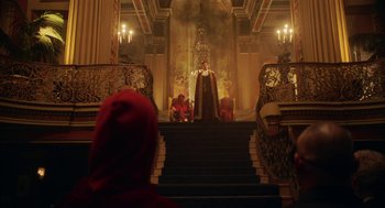 Movie still from “House Party” (2023), directed by Calmatic – A man in a red hooded jacket sitting in front of a throne; Extreme Wide shot, Low angle