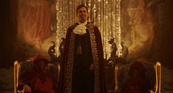 Movie still from “House Party” (2023), directed by Calmatic – A man wearing a robe and a cape standing in front of a painting; Wide shot, Over the shoulder angle