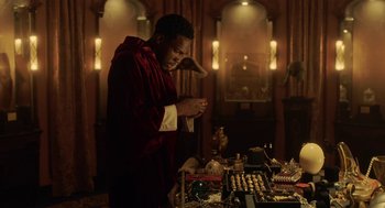 Movie still from “House Party” (2023), directed by Calmatic – A man standing in front of a table with many items; Medium shot, High angle