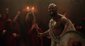 Movie still from “House Party” (2023), directed by Calmatic – A man in chains is holding a stick; Medium shot, Low angle