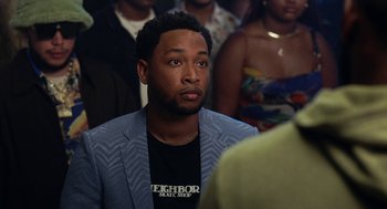 Movie still from “House Party” (2023), directed by Calmatic – A man in a blue jacket is sitting in front of a group of people; Close Up shot, Over the shoulder angle