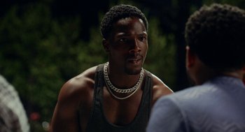 Movie still from “House Party” (2023), directed by Calmatic – A man wearing a chain around his neck looks into the distance; Close Up shot, Over the shoulder angle
