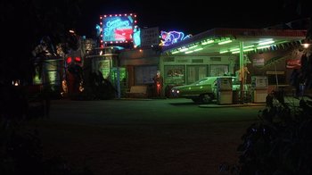Movie still from “House of 1000 Corpses” (2003), directed by Rob Zombie – A car parked in front of a gas station at night; Extreme Wide shot, High angle