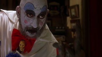 Movie still from “House of 1000 Corpses” (2003), directed by Rob Zombie – A man with a clown makeup on his face; Close Up shot, Over the shoulder angle
