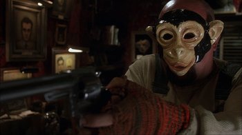 Movie still from “House of 1000 Corpses” (2003), directed by Rob Zombie – A person wearing a monkey mask and holding a gun; Close Up shot, Over the shoulder angle