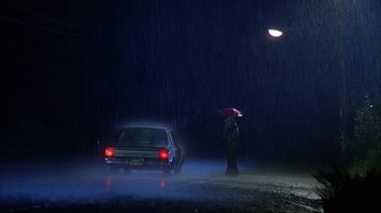Movie still from “House of 1000 Corpses” (2003), directed by Rob Zombie – A person standing in the rain holding an umbrella; Extreme Wide shot, Low angle