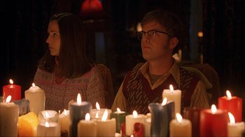 Movie still from “House of 1000 Corpses” (2003), directed by Rob Zombie – A man and a woman sitting in front of candles; Medium shot, Over the shoulder angle