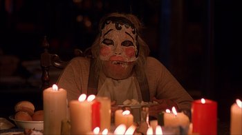 Movie still from “House of 1000 Corpses” (2003), directed by Rob Zombie – A person with a face paint sitting in front of a table of candles; Close Up shot, Over the shoulder angle