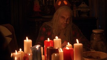 Movie still from “House of 1000 Corpses” (2003), directed by Rob Zombie – A man sitting in front of a group of candles; Medium shot, High angle