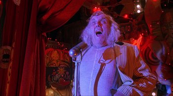 Movie still from “House of 1000 Corpses” (2003), directed by Rob Zombie – A man with a long white beard is singing into a microphone; Medium shot, Low angle