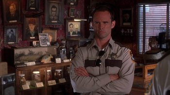 Movie still from “House of 1000 Corpses” (2003), directed by Rob Zombie – A police officer standing in front of a wall of pictures; Close Up shot, Over the shoulder angle