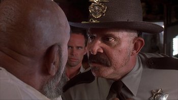 Movie still from “House of 1000 Corpses” (2003), directed by Rob Zombie – A man in a police uniform is looking at another man in a uniform; Close Up shot, Over the shoulder angle