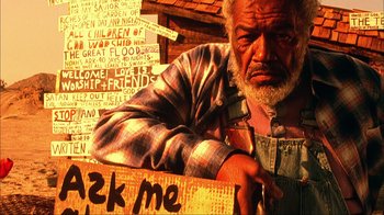 Movie still from “House of 1000 Corpses” (2003), directed by Rob Zombie – An old man with a beard and plaid shirt holding a sign; Medium shot, Low angle